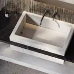 Modern rectangular stone sink with wall-mounted faucet, soap dispenser, and minimalist countertop design.