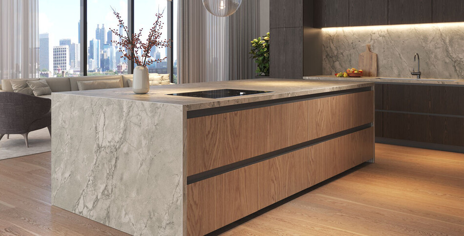Luxury kitchen island of Transcenda porcelain with a gray veined stone waterfall edge and wood cabinets, set against floor-to-ceiling windows with a city skyline view.