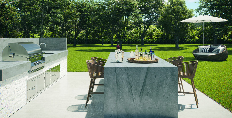 Outdoor kitchen and bar area with a seamless dark gray Monumental porcelain waterfall countertop island and an integrated grill station with white brick on a patio.