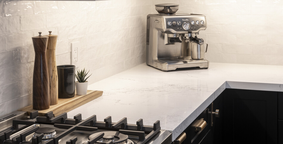 A gas stovetop and espresso maker on an Empira White quartz countertop.