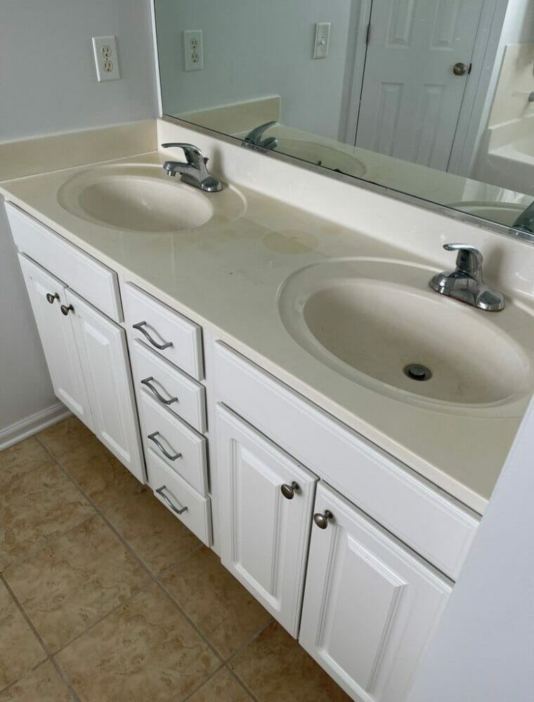 Bathroom before a makeover with dirty plastic countertops and white cabinets.