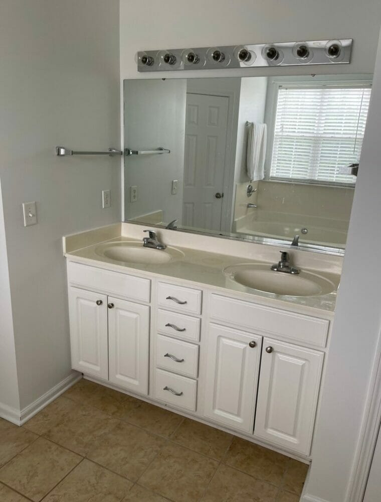 Full bathroom vanity before shot. Shows old plastic countertop, white cabinets, large single mirror, and open bulb light fixture.