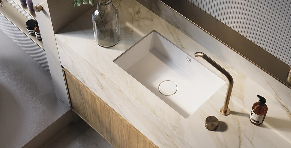 A luxury bathroom vanity top crafted from Mirabel porcelain with warm, light-gold veining, featuring an undermounted white sink and a modern brushed brass faucet.