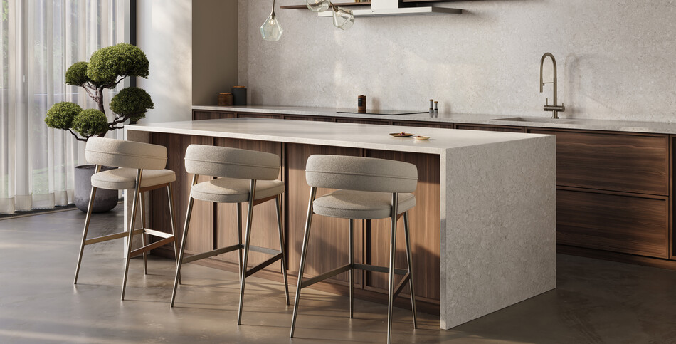 Contemporary kitchen featuring a large waterfall island and matching backsplash of light-gray patterned Fossillia porcelain, complemented by wooden cabinetry and modern bar stools.